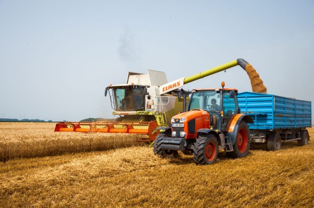 A modern tractor and harvester working in a wheat field during the summer harvest.